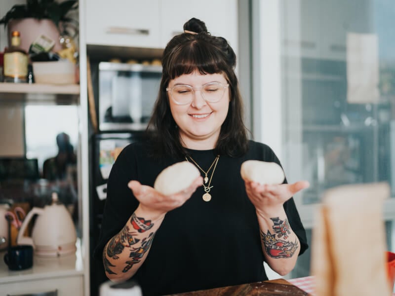 A woman holds handmade dough balls at a virtual pizza making class